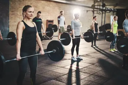 Group of strong male and female adults holding heavy barbells in ftness exercise studio with thick mats on floor and brick walls