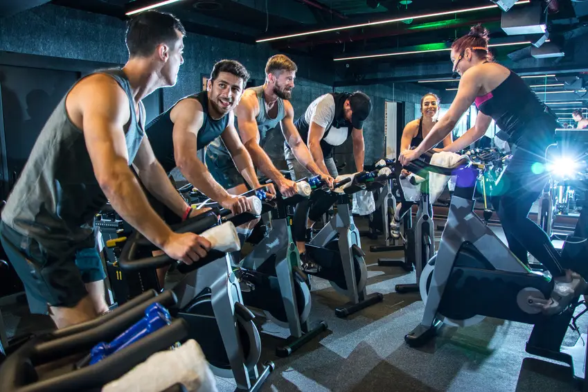 Group of happy sporty people riding spinning bikes together in gym.